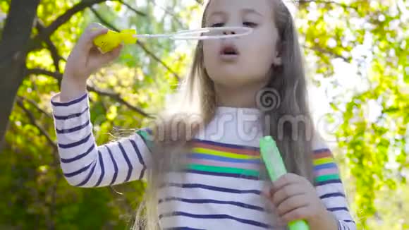 一个漂亮的黑发女孩在秋天的阳光和吹肥皂泡的特写镜头穿条纹夹克的小孩视频的预览图