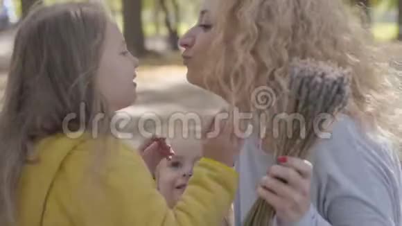 特写两个小白种人女孩亲吻他们的母亲和嗅花的肖像漂亮的金发卷发女人视频的预览图