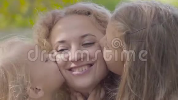 两个漂亮的白种人女孩亲吻母亲脸颊的特写照片快乐的姐妹们表达了视频的预览图