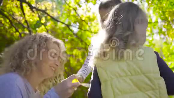 微笑着的金发白种人女人卷发坐在阳光下和她漂亮的小女孩玩肥皂泡视频的预览图