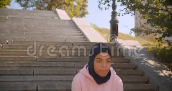 年轻的动机吸引人的非裔美国穆斯林女孩戴头巾在城市楼梯上做有氧运动的特写照片视频的预览图