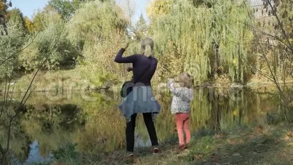 一个女人和一个小女儿一起在池塘边的秋天公园里快乐地跳舞视频的预览图