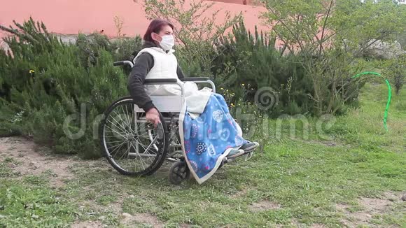 残疾妇女独自坐在轮椅上戴着防护面罩在花园里呼吸一些空气被隔离使一切正常视频的预览图