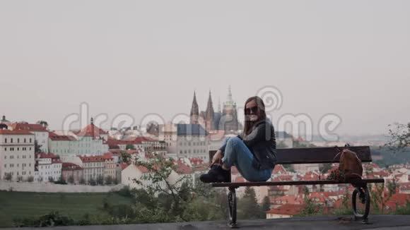 戴墨镜的快乐女孩坐在长凳上捷克传统屋顶的背景视频的预览图