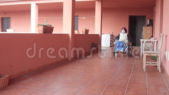 残疾妇女独自坐在轮椅上带着防护面罩朝阳台走去观看风景视频的预览图
