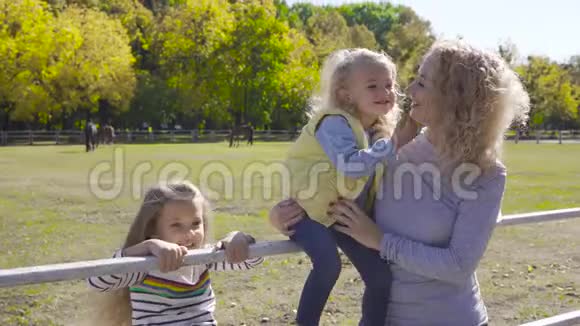 两个可爱的小妹妹和他们可爱的妈妈一起在畜栏旁边快乐的白种人家庭花时间视频的预览图