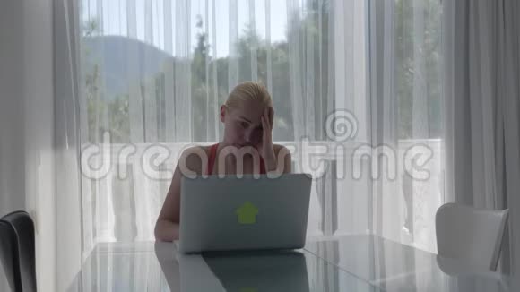 一个女人坐在一个大窗户前的桌子前有一个美丽的森林景观在笔记本电脑上工作视频的预览图
