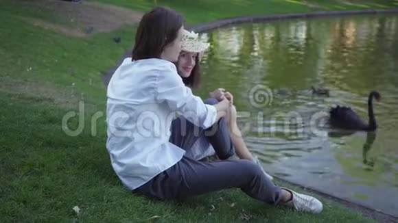 一对幸福的夫妇坐在湖边或河畔谈笑风生年轻的白人男女花时间视频的预览图