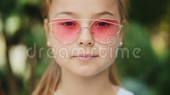 户外戴粉色太阳镜的年轻微笑女孩特写视频的预览图