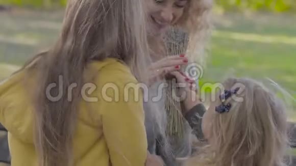 两个可爱的高加索小姐妹给妈妈送花和亲吻她的特写漂亮的金发卷发视频的预览图