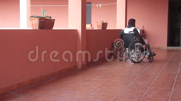 残疾妇女独自坐在轮椅上带着防护面罩朝阳台走去观看风景视频的预览图