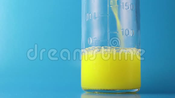 黄色液体倒入深蓝背景的玻璃量瓶中的照片视频的预览图