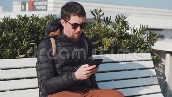 坐在长凳上的智能手机上戴太阳镜的游客视频的预览图
