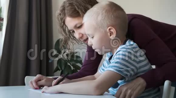 孩子坐在家里的桌子上和他们的妈妈一起画画家庭概念视频的预览图