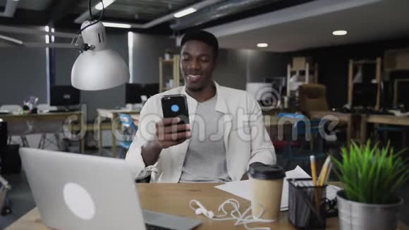 美国黑人年轻人在办公室微笑并使用电话视频的预览图