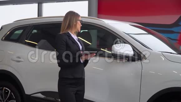 女卖家站在汽车经销商的旁边在平板电脑上做笔记视频的预览图