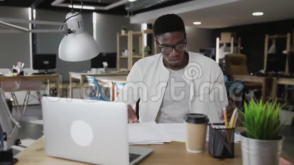 年轻貌美的非洲男人戴着眼镜坐在办公室的桌子上拿着文件视频的预览图