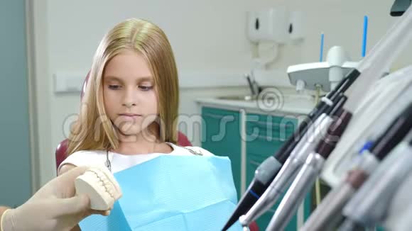牙医在牙医办公室展示小女孩下巴模型孩子的牙科治疗坐在诊所的牙科椅上视频的预览图
