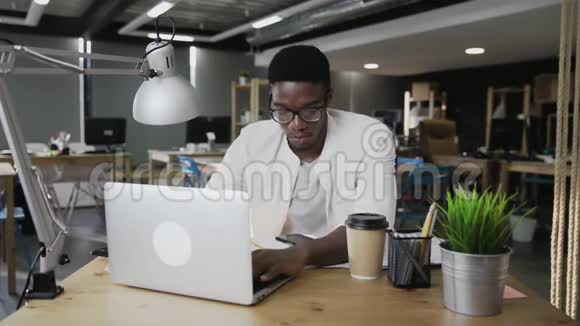 非洲商人正在用笔记本电脑工作并在现代办公室接听电话视频的预览图