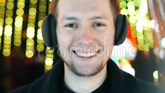 年轻开朗的男子肖像带着温暖的耳机微笑看着相机圣诞花环的灯光视频的预览图
