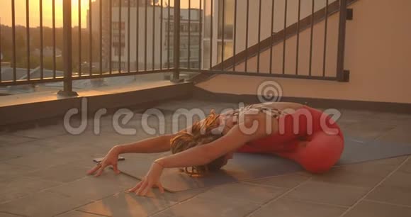 在屋顶上练习瑜伽莲花的女伴用美丽的城市风景日落特写视频的预览图