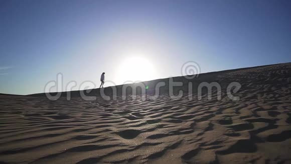 一个静止的镜头从远处一个女性的剪影走在沙漠中的沙丘上在日落时经过太阳自由和自由视频的预览图
