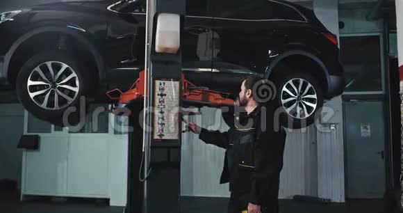 成熟的汽车修理工在现代汽车服务中把汽车举起来检查汽车悬架视频的预览图
