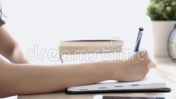 特写亚洲女人坐在家里的书桌上学习写笔记本和日记视频的预览图