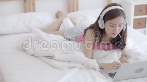 美丽的年轻亚洲女人微笑着用聊天社交网络打招呼卧室里有笔记本电脑视频的预览图
