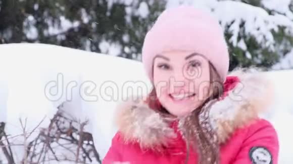 在一个阳光明媚的冬天穿着红色夹克的年轻女子微笑着向空中扔雪视频的预览图