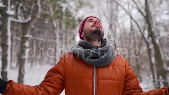 在圣诞节假期的寒假里在户外享受降雪的嬉皮士男子快乐的家伙在雪地里张开双臂视频的预览图