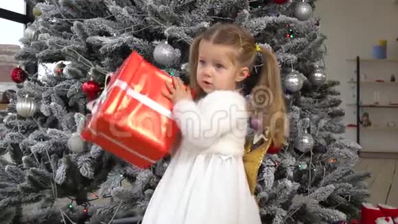 小女孩摇晃着红色的礼盒试图了解里面的东西视频的预览图