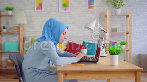 年轻的穆斯林妇女戴着传统的头巾坐在笔记本电脑前感到脖子疼痛视频的预览图