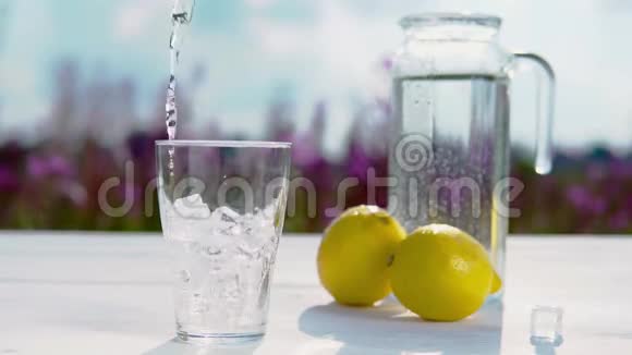 一只手把水倒进一个空杯子里里面有冰块立在一张白色的桌子上旁边有一个水和两个水的装饰器视频的预览图