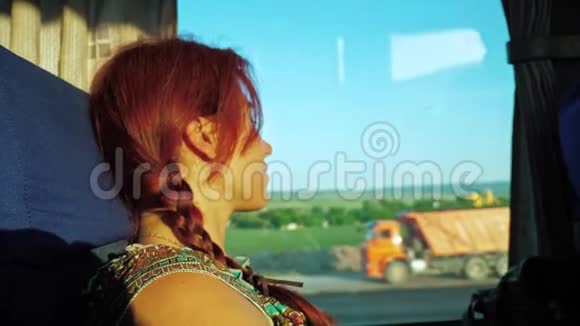 一个孤独的红发旅行女孩看着公共汽车窗外的道路运输自然和蓝天视频的预览图