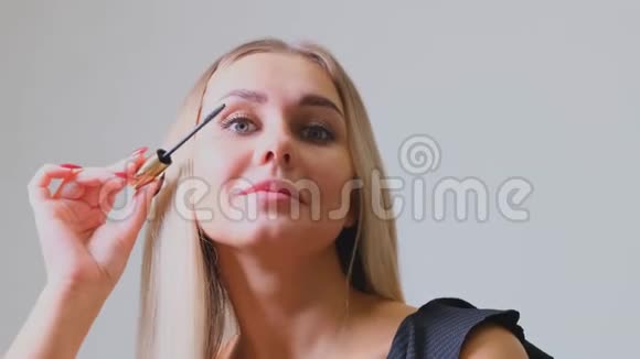 漂亮的金发女人在镜子前的睫毛上涂上睫毛膏美容和化妆概念视频的预览图