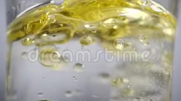 美丽的镜头靠近液体在一杯水中黄色的油倒进一罐清水和气泡中视频的预览图