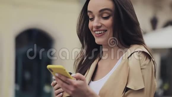 年轻迷人的女孩看起来真的很印象深刻使用她的手机笑说哇持有Cofe杯打字和视频的预览图