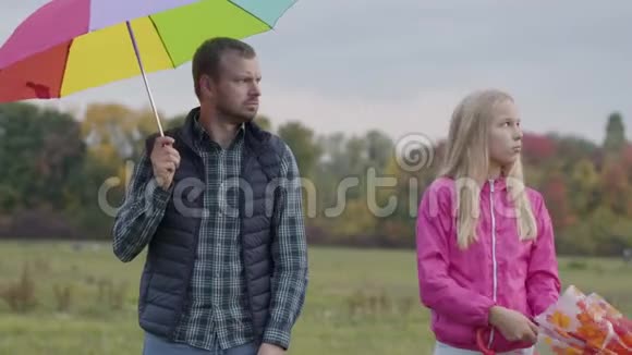 成年白种人男子和金发少女站在多种颜色的雨伞和等待雨父亲和视频的预览图