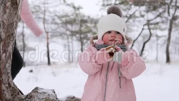 穿着粉红色冬季连衣裙的小女孩在雪天上雪橇后吃圣诞姜饼可爱的家庭过冬视频的预览图
