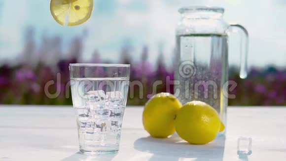 手把一片柠檬放在一杯水上冰站在一张白色的桌子上背景是一杯十色的水视频的预览图