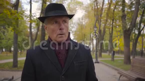 一位戴着优雅黑帽和外套的白发老者的特写在小巷中漫步视频的预览图