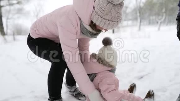 母亲在雪地里养育孩子穿暖和连衣裙的孩子学会走路在冬天森林里走第一步的女孩视频的预览图