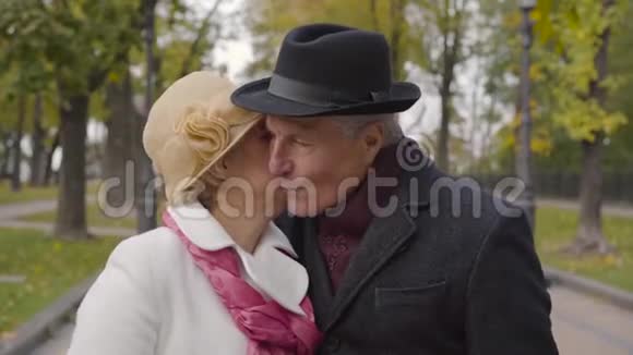 一个成熟的高加索女人戴着优雅的克洛切帽子和白色外套亲吻她可爱的丈夫的脸颊高级视频的预览图