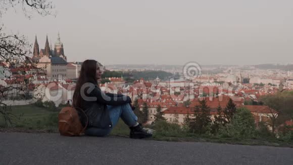 漂亮的女孩穿着牛仔裤和靴子的背包体贴地坐在观察甲板上可以看到布拉格女孩视频的预览图