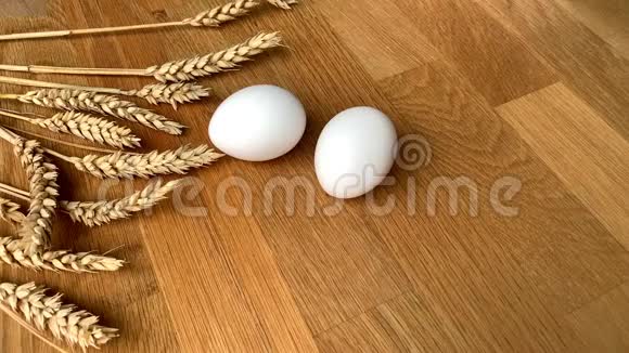 两个白色的鸡蛋躺在木桌上一根小小的羽毛落在上面贴着成熟的麦穗视频的预览图