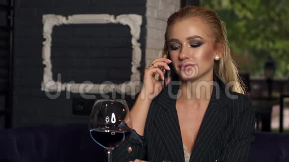 年轻的女人独自坐在酒吧里打电话喝红酒视频的预览图