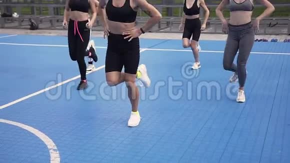 运动短上衣和运动短裤的性感女教练向她的健身小组展示跳腿练习视频的预览图