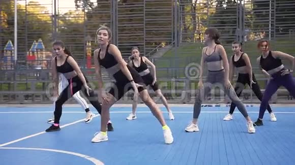 女子健身队与教练在公园的运动场上进行日间蹲式练习视频的预览图