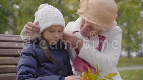 高加索族妇女戴着米黄色的克洛切帽子穿着白色外套为孙女的白帽子做着固定奶奶快乐视频的预览图